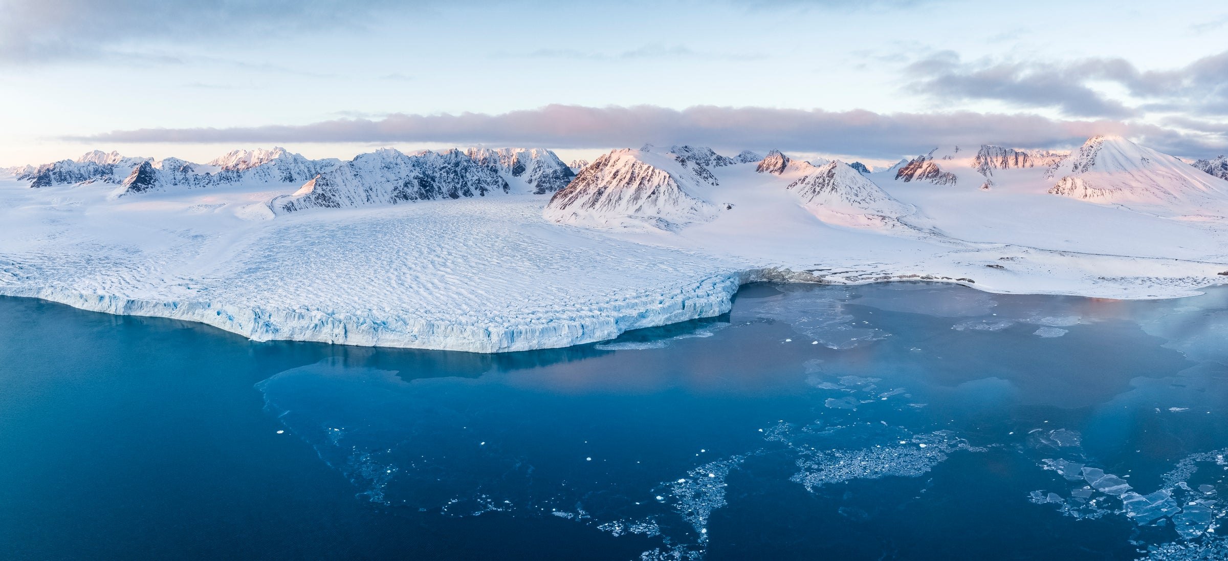 A glacier meeting a still fjord, mountains in blue morning light