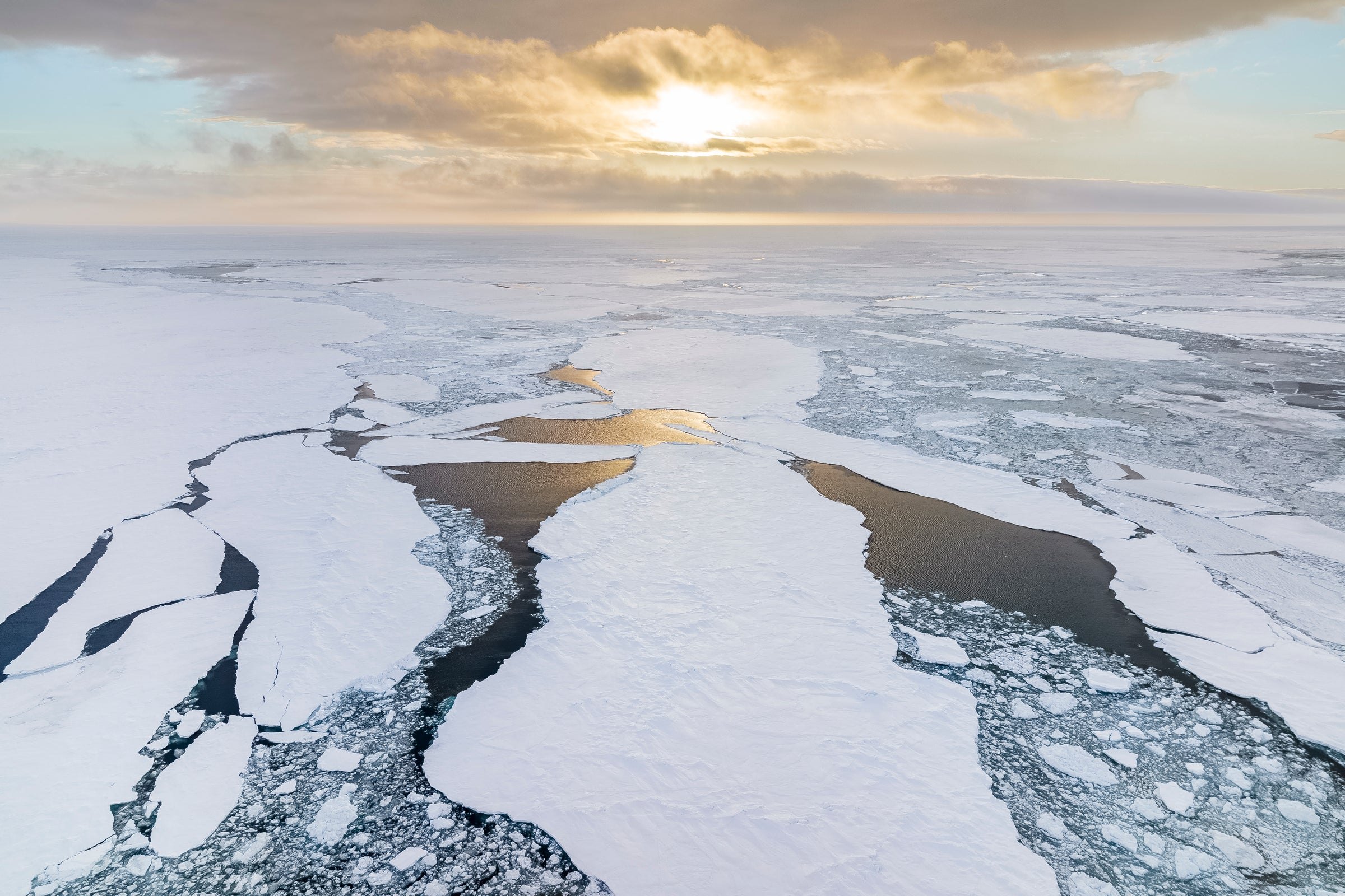 Sea ice breaking into floes and open leads beneath a low sun