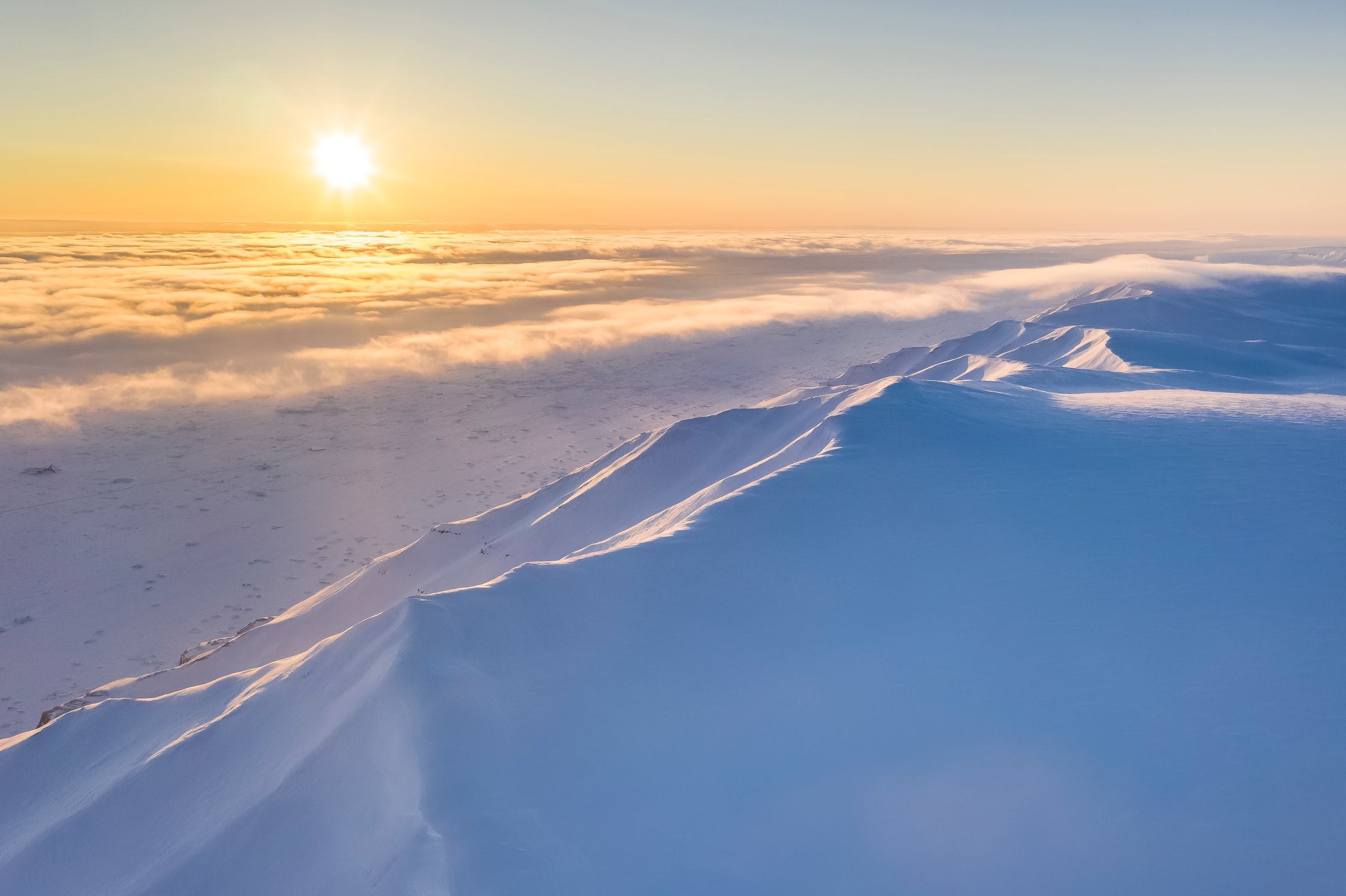 A snow-covered ridge above a layer of cloud, the sun low over the horizon