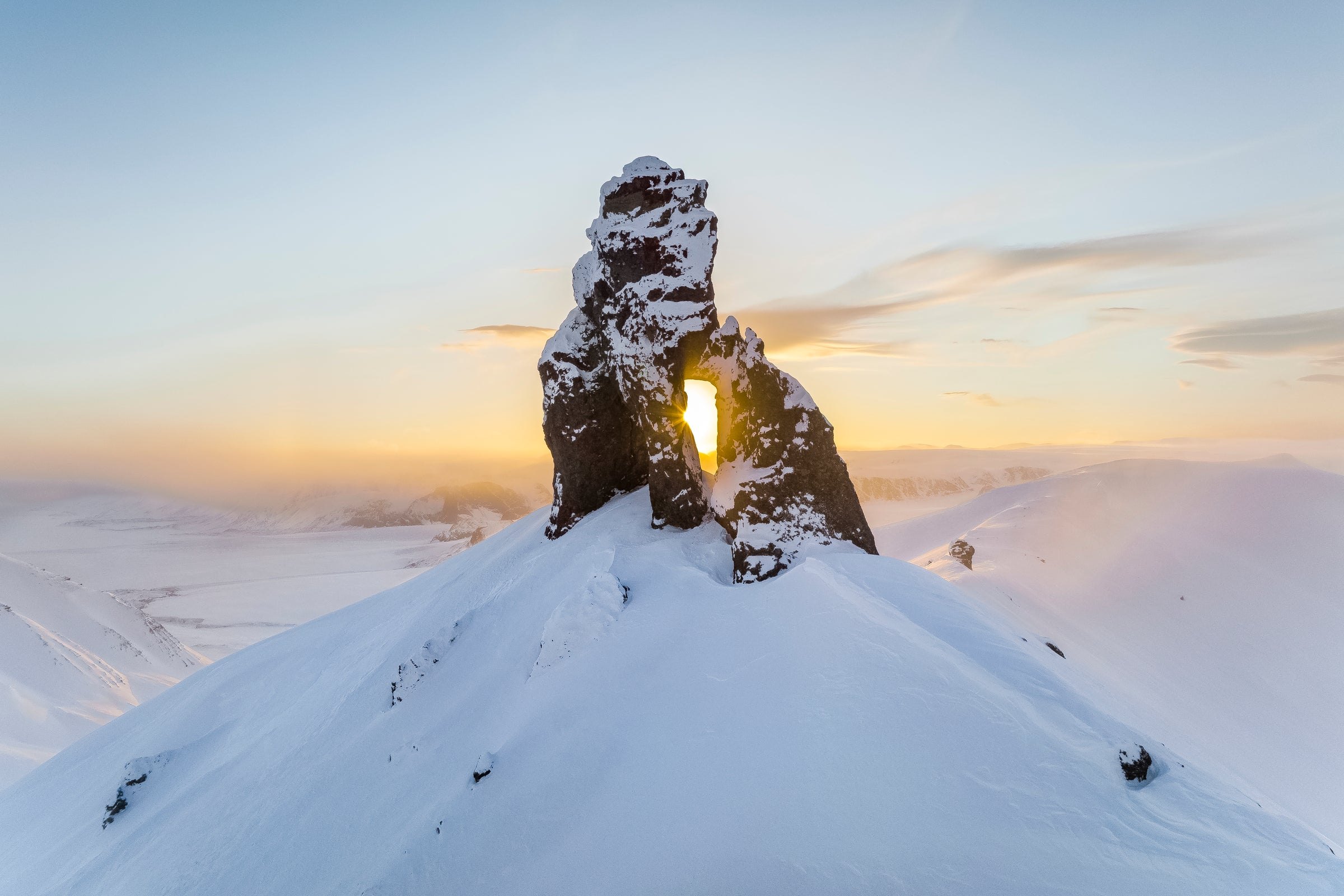 A stone arch on a snow-covered summit with the sun shining through the opening